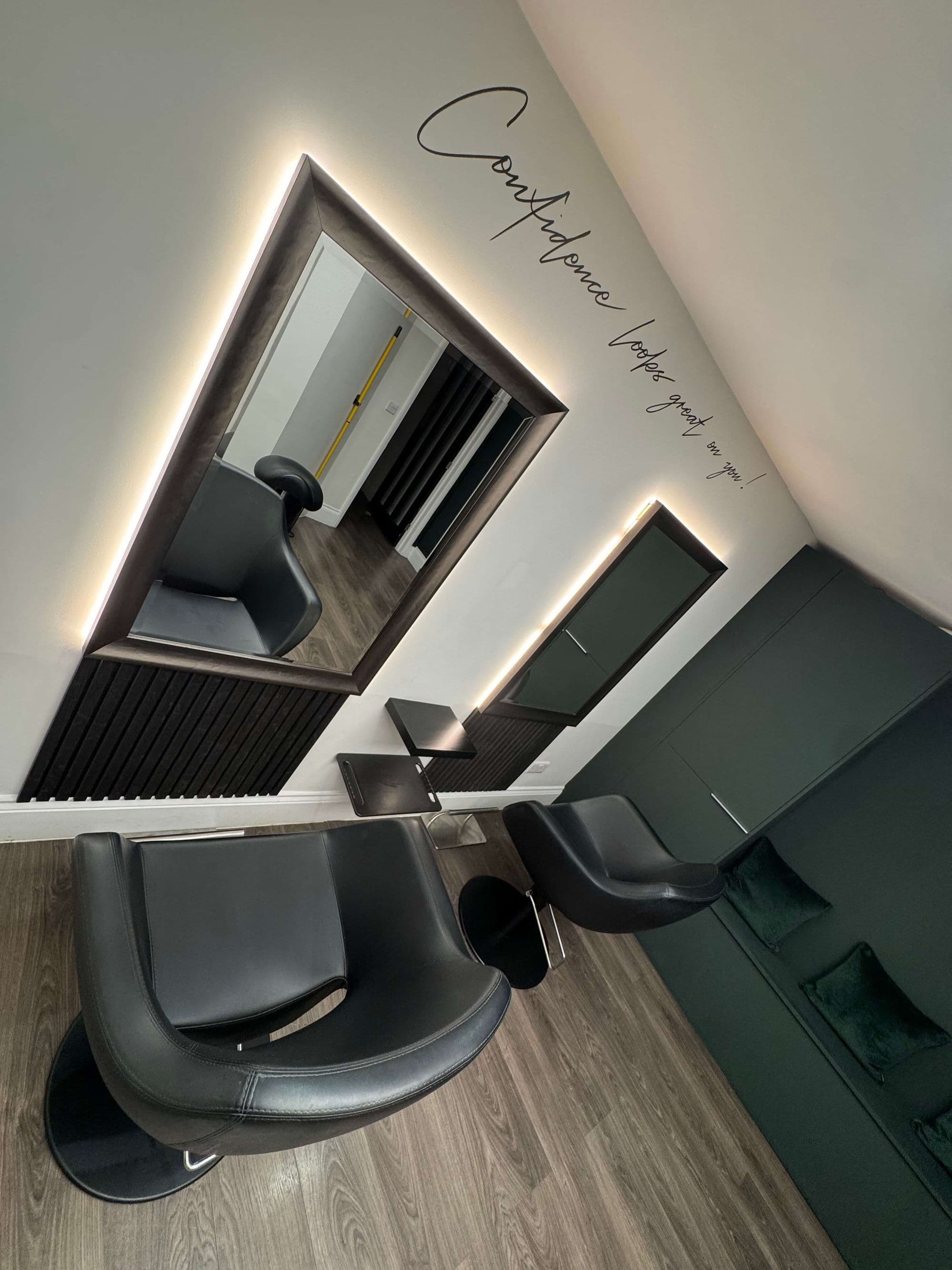 A Clay styling corner, lit mirror and chair beneath the salon’s wall lettering